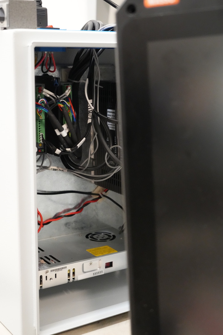 An open white control cabinet showing its wiring, drivers, and power supply